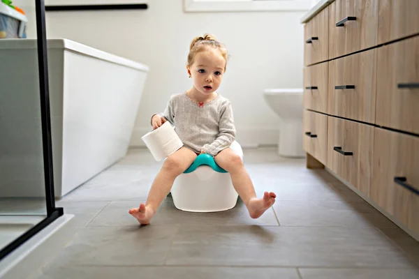 Schattig jong baby zitten en leren hoe het toilet te gebruiken met wc-papier op de hand Stockfoto