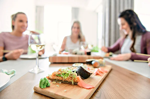 Focus on sushi with a Group of attractive mature people eating sushi at home on the back —  Fotos de Stock