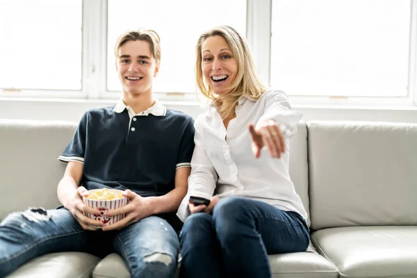 A people and family happy teen boy with mother on sofa at home listening TV — ストック写真