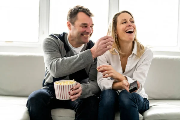 A Happy young couple lying on the sofa at home with popcorn watching TV — Photo