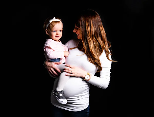 A portrait of beautiful pregnant mother with her little daughter girl over dark background. — ストック写真