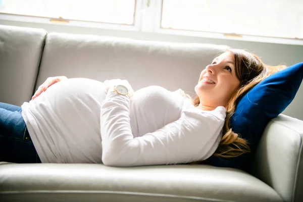Una mujer embarazada feliz tumbada en el sofá en casa —  Fotos de Stock