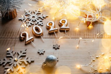 Altın 2022 mum numaraları Noel süslemeleri ve Noel ışıkları ile ahşap zemin üzerinde bohçalanır.