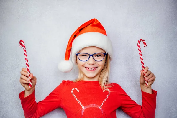 Щаслива маленька дівчинка в окулярах і капелюсі Санта і тримає цукерки під час різдвяних і новорічних свят. — стокове фото