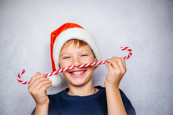 Грайливий хлопчик з Санта-Капелюха робить вуса цукерками під час різдвяних та новорічних свят. — стокове фото