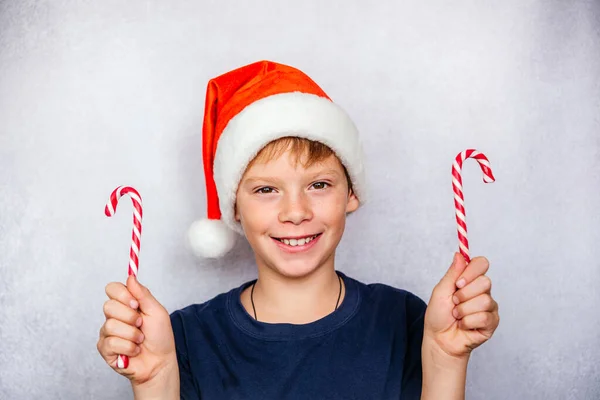 Menino brincalhão em chapéu de Papai Noel segurando bengalas doces durante o Natal e feriados de Ano Novo — Fotografia de Stock