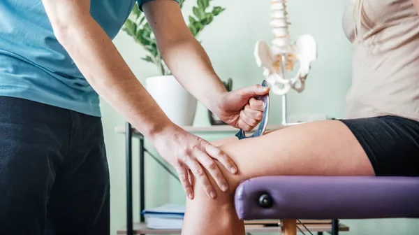 Therapist using IASTM instrument treatment, girl receiving soft tissue treatment on her leg with guasha stainless steel tool — Stock Photo, Image