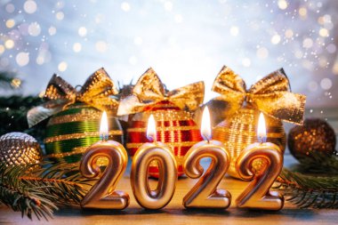Mutlu yıllar 2022, altın sayılar 2022 yanan mum, altın fiyonklu Noel ağacı topları ve Noel ışıkları bokeh