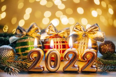 Mutlu yıllar 2022, altın sayılar 2022 yanan mum, altın fiyonklu Noel ağacı topları ve Noel ışıkları bokeh