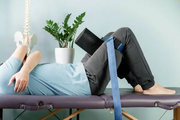 A man lying on the massage table in constructive rest postion with foam roller and malligan belt — Stock Photo, Image