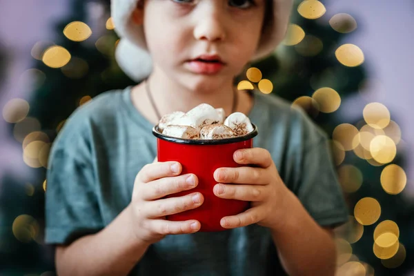 Маленький хлопчик у Санта-Капелюшці з чашкою гарячого шоколаду з зефіром. — стокове фото