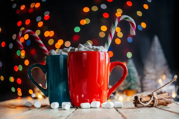 Rote und grüne Tassen mit heißer Schokolade mit Eibisch und Zuckerstangen auf weihnachtlichem Hintergrund — Stockfoto