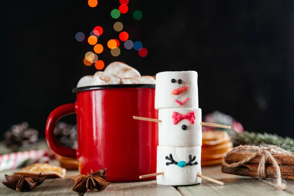 Red enamel mug of hot chocolate with marshmallow snowman on Christmas background — Stock Photo, Image