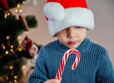 Noel Baba şapkalı küçük çocuk Noel zamanı şeker çubuğu lolipop yiyor.