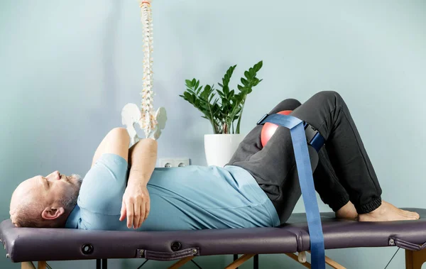 A man lying on the massage table in constructive rest postion with foam roller and malligan belt — Stock Photo, Image