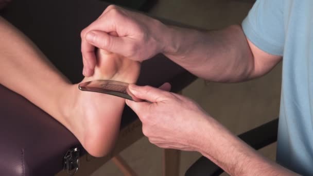 Физиотерапевт, устраняющий боль в пятках с помощью гуаши инструмента IASTM — стоковое видео