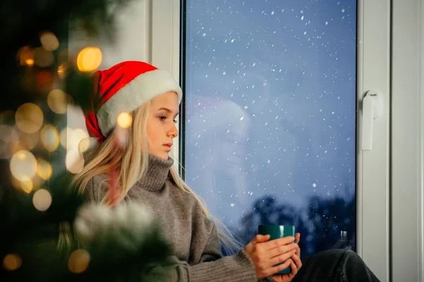 Молода дівчина-підліток у капелюсі Санта має чашку гарячого напою з ялинкою на передньому плані — стокове фото
