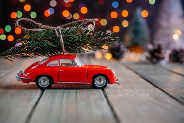 Noel arkaplanında köknar ağacı ve renkli Noel ışıkları olan minyatür kırmızı bir araba.