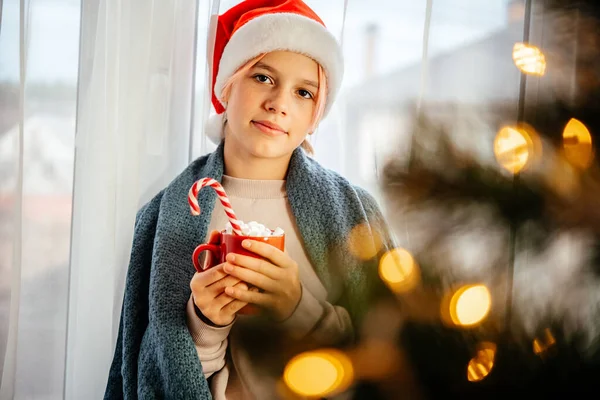 Затишне Різдво вдома святковий фон з дівчиною в капелюсі Санта та чашкою гарячого шоколаду — стокове фото