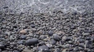 Boş bir çakıl taşlı sahilde köpüklü deniz dalgaları