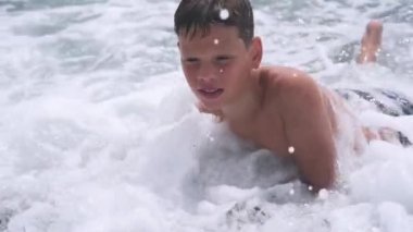 Köpüklü deniz dalgalarında yüzen bir çocuk çakıllı deniz kıyısına çarpıyor.