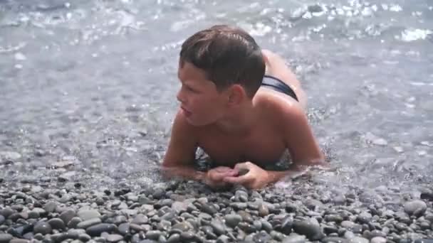 Ein Junge schwimmt in den schäumenden Meereswellen, die auf den Kiesstrand treffen — Stockvideo