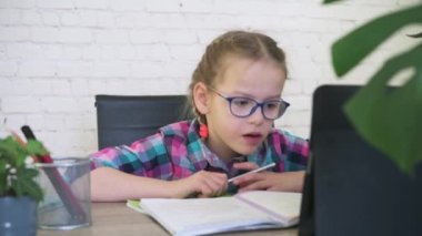 Gözlüklü kız tabletine bakıyor ve internetten ders alırken not alıyor.