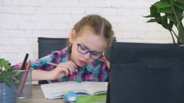 Gözlüklü kız tabletine bakıyor ve internetten ders alırken not alıyor.