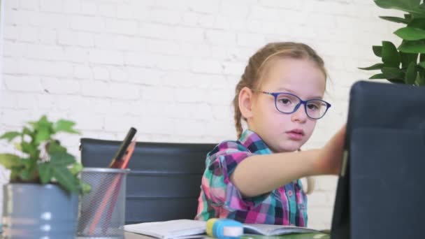 Menina em óculos estudando on-line em casa, uma menina da escola primária com computador tendo zoom vídeo chat com professor — Vídeo de Stock