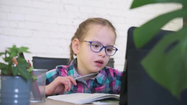 Κορίτσι του δημοτικού σχολείου με γυαλιά ηλίου που γράφει στο σημειωματάριό της, ενώ έχει online μάθημα κατά τη διάρκεια του αποκλεισμού covid, εξ αποστάσεως εκπαίδευση για τα παιδιά — Αρχείο Βίντεο