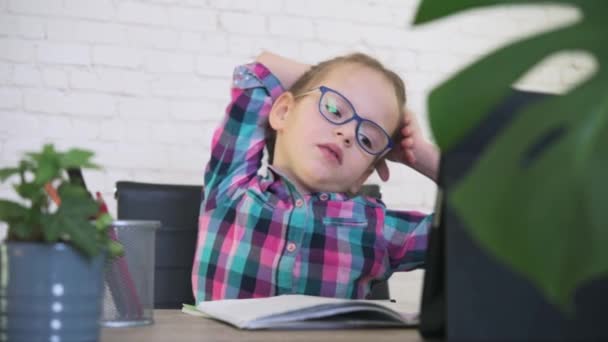 Trött liten flicka i glasögon sträcker ut armarna samtidigt som hon har online lektion, distansundervisning för barn — Stockvideo