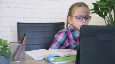 Gözlüklü kız tabletine bakıyor ve internetten ders alırken not alıyor.