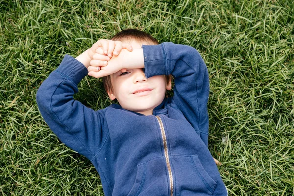 Lindo niño mintiendo sobre hierba verde en el parque — Foto de Stock