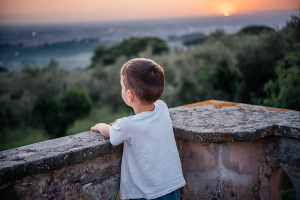 Vista posterior de un pequeño niño mirando la hermosa puesta de sol sobre el olivar en el paisaje montañoso de Italia — Foto de Stock