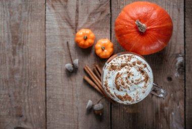 Autumn pumpkin spicy drink, pumpkin latte on wooden background top view, autumn vegan latte with spices, cinnamon, and stars of anise