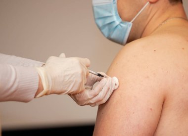 Bir insana omzuna şırınga enjekte edilir. Coronavirus aşısı. Tehlikeli enfeksiyonların aşılanması ve tedavisi.