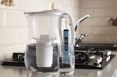 Suyun TDS 'sinin ölçümü. Elektronik pH metre ve bir bardak su. Su arıtma için filtre. Arka planda içme suyu musluğu var.. 