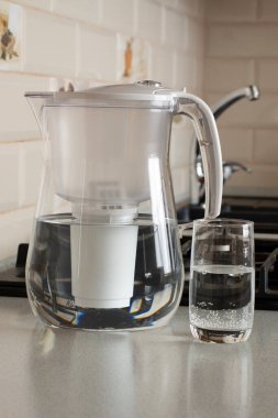 Mutfakta bir bardak temiz suyla filtre yapın. Arka planda lavabo ve musluk var. Arındırılmış su kavramı. (Tercümesi: tatlım, ben)