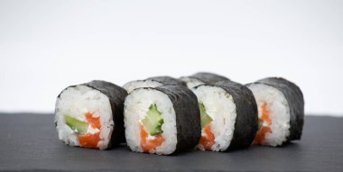 Siyah bir stantta somonlu suşi rulosu ve beyaz bir arka plan.