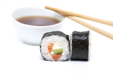 Beyaz bir zemin üzerinde somonlu suşi rulosu ve Japon yemek çubukları ve çalılıklarda sos.