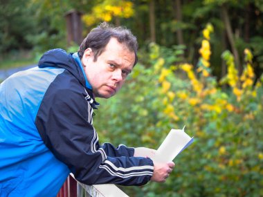 Mavi ceketli adam kötü haberlerle mektup okuyor ve sonbahar doğasında korkuluklara yaslanıyor.