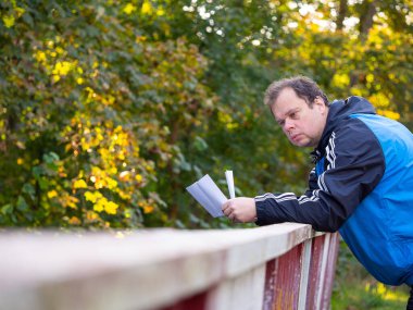 Mavi ceketli adam kötü haberlerle mektup okuyor ve sonbahar doğasında korkuluklara yaslanıyor.
