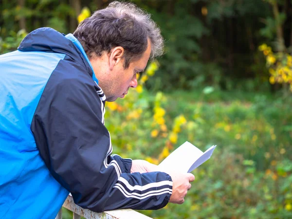 Man in blue jacket reading letter with bad news and leaning on the railing in autumn nature