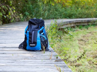 Sırt çantası ahşap yolda, sonbahar doğasında siyah ve mavi bir çanta.