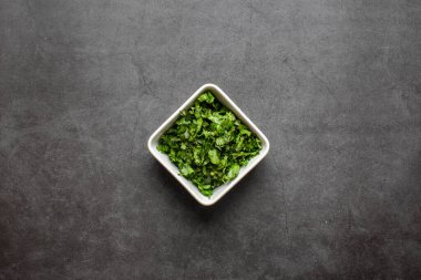 Koyu gri arka planda beyaz tabakta doğranmış taze kişniş yaprakları. en üstteki görünüm.