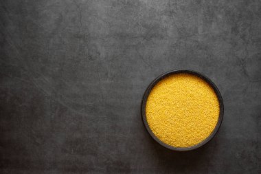 Sarı darı kaşıkta ve kase koyu gri arka planda.