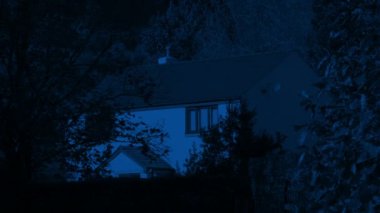 Geceleri rüzgarda hareket eden ağaçlarla dolu bir ev.