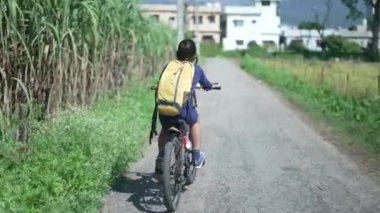 Hintli bir çocuk Uttarakhand, Hindistan kırsalındaki şeker kamışı tarlasının yanında bisiklet sürüyor..