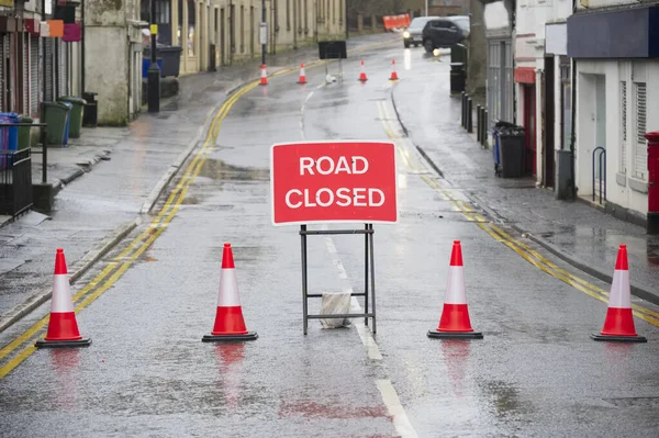 Road ahead closed sign with traffic cones and red barrier fence crossing
