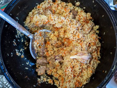 National Uzbek dish pilaf, pilaw, plov. Rice, onion, carrot, garlic and meat in a cauldron.